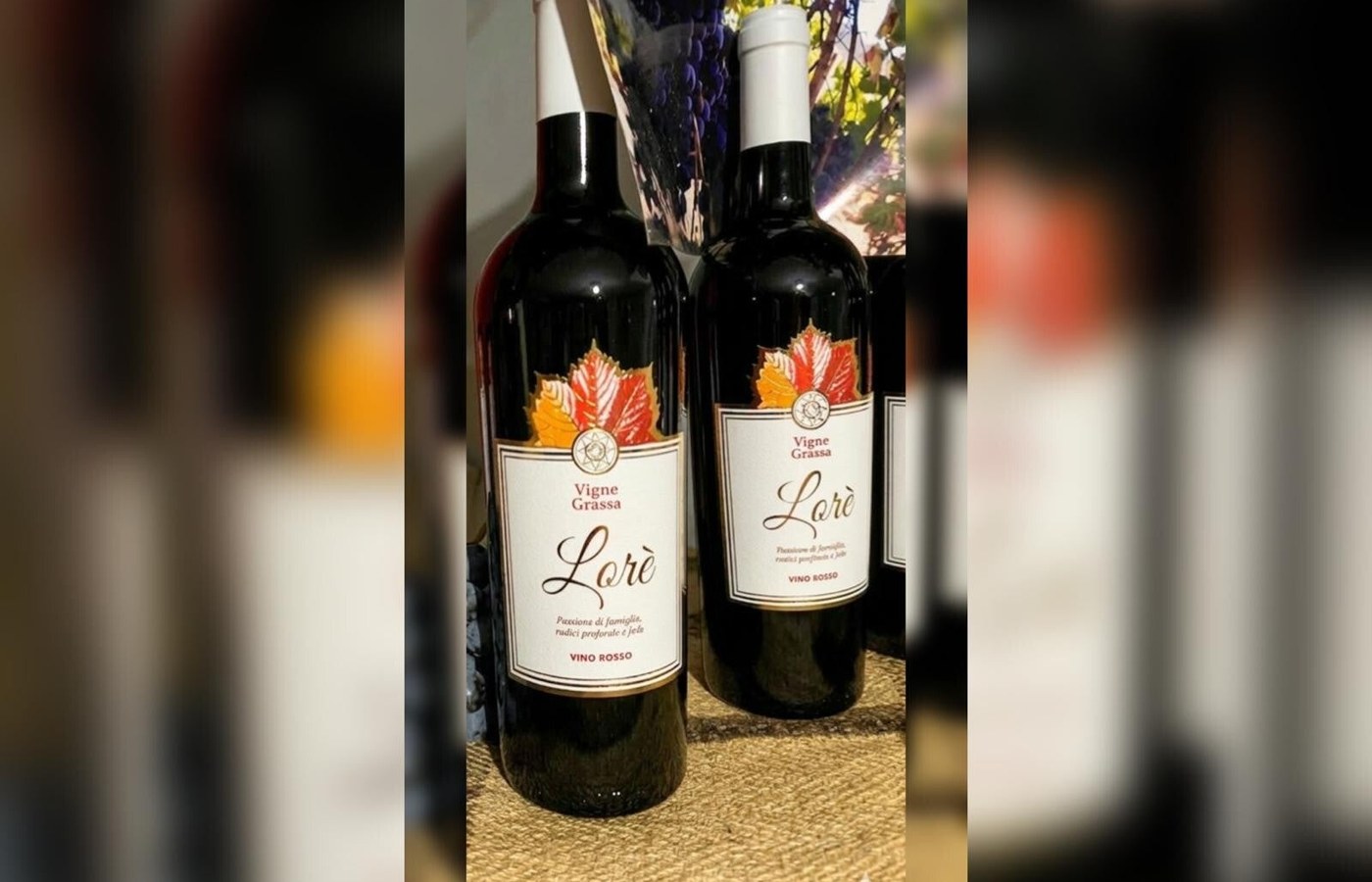 Bottiglie di vino rosso Lorè Vigne Grassa con etichetta bianca e foglia di vite autunnale, su tela di juta e uva nera